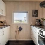 Küche mit weißen Schränken, dunklem Arbeitsplatz und Holzwand. Fenster mit Blick nach draußen.