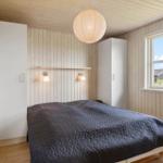 Schlafzimmer mit Bett, weißen Schränken und Holzwand. Fenster zeigt Landschaft.