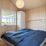 Schlafzimmer mit Holzwand, Bett mit blauer Bettdecke und Fenster mit Blick nach draußen.