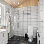 Badezimmer mit Dusche, Toilette und Waschbecken. Holzdecke und weiße Fliesen.