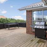Terrasse mit Grill, Tisch und Holzbelag. Blick auf Grünflächen und Haus.