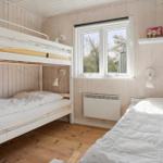Zimmer mit Doppelstockbett und Einzelbett, Holzwand und Fenster.