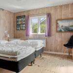 Zimmer mit zwei Betten, Holzwand, Fenster, Stuhl und Wandbild.