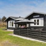 Holzhaus mit Terrasse, Sonnenschutz und Garten. Spielplatz im Hintergrund.