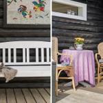 Weiße Bank mit Decke vor Holzwand. Tisch mit Stühlen und Blumen auf Terrasse.