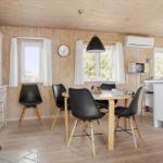 Essbereich mit Tisch, Stühlen und Küchenzeile. Holzwände, Fenster und Kaminofen.