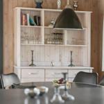 Esstisch mit Stühlen und Sideboard mit Gläsern und Büchern.