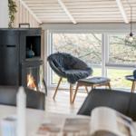 Ein Raum mit Holzdecke, Kamin und Sessel vor großem Fenster.