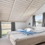 Schlafzimmer mit Doppelbett, Holzdecke und Fenstern mit grauen Vorhängen.