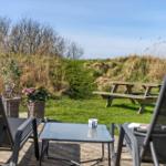 Terrasse mit Liegestühlen und Tisch. Hintergrund: Grasfläche und Picknicktisch.