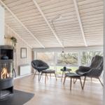 Wohnraum mit Kamin, Sitzgelegenheiten und großem Fenster. Holzdecke und -boden.