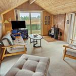 Wohnzimmer mit Holzdecke, Sofa, Sessel, Kamin und TV. Blick auf Terrasse.