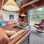 Living room with brown sofa, armchair, and large window. Wooden ceiling and wall pictures.