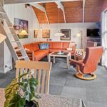 Living area with orange sofa, wooden ceiling, and staircase.