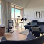 Living room with sofa, chairs, and balcony view. TV, pictures, and telescope visible.