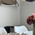 Dining table with flower vase and modern lamp. Background: chair and wall shelf.