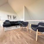 Living room with sofa, two armchairs, and wooden floor under sloped walls.