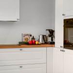 Küche mit weißen Schränken, Holzoberfläche und eingebauter Backofen.