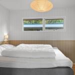 Schlafzimmer mit Doppelbett, weißen Wänden und Holzverkleidung. Fenster und Deckenleuchte sichtbar.