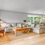Wohn- und Essbereich mit Sofa, Sessel und Holztisch. Holzfußboden und große Fenster.