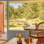 Durch die Tür blickt man auf eine Terrasse mit Stuhl und Tisch. Im Hintergrund sind Bäume und Gras sichtbar.