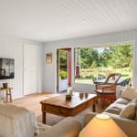 Wohnzimmer mit Sofa, Couchtisch und Fernseher. Große Fenster mit Blick auf Garten.