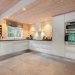 Moderne Küche mit weißen Schränken, Holzwand und -decke, integriertem Ofen und Fenster.