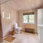 Badezimmer mit Holzwand, Toilette, Waschbecken und Fenster mit Blick auf Grün.