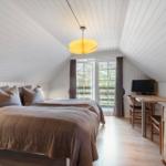 Schlafzimmer mit Doppelbett, Schreibtisch und TV. Holzdecke und Fenster zur Terrasse.