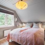 Schlafzimmer mit Dachschräge, Bett mit rosa Bettwäsche, Fenster mit Blick auf Bäume.