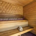 Sauna mit Holzbank, geometrischer Wandverkleidung und gefalteter Handtuchrolle.