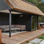 Hütte mit Holzterrasse, Dach aus Stroh und Außensitzbereich mit Sofa.