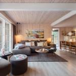Wohnzimmer mit Sofa, Tischen und Fenstern. Küche und Treppenhaus im Hintergrund.