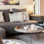 Ein Wohnzimmer mit grauem Sofa, dekorativen Kissen und zwei runden Tischen.