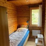 A bedroom with wooden walls, bed, window, and chair.