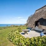 Haus mit Strohdach und Terrasse mit Blick auf Meer und Grünflächen.
