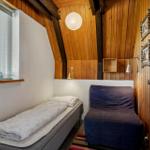 Ein Schlafzimmer mit Bett, Sessel und Holzwand. Fenster mit Jalousie und Deckenleuchte.