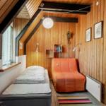 Schlafzimmer mit Bett, orangefarbenem Sessel und Holzwandverkleidung unter Dachschräge.