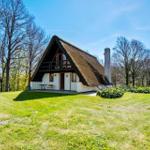 Haus mit Strohdach, Garten und Bäumen unter blauem Himmel.
