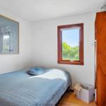 Schlafzimmer mit Bett, Fenster und Holzschränkchen