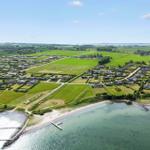 Aerial view of coastal village with green fields, houses, and water docks.