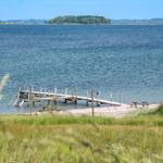 Holzsteg führt zum Wasser. Picknicktisch und Strand im Vordergrund.