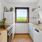 Küche mit Holzoberflächen, weißer Einbauküche und Fenster mit Blick auf Grün.