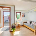 Wohnraum mit Sofa, Tisch und Blumen. Durchgang zur Terrasse mit Grill.