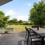 Terrasse mit Tisch und Stühlen, Blick auf Grünfläche und Bäume unter blauem Himmel.