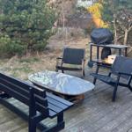 Terrasse mit Tisch, zwei Stühlen und Bank. Grill und Lichterkette im Hintergrund.