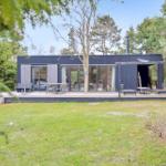 Moderne schwarze Hütte mit Terrasse, Garten und Bäumen. Große Fenster und Außensitzgelegenheiten.