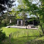 Moderne Villa mit Terrasse, Garten und Grillplatz unter Bäumen.