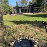Haus mit Terrasse und Grillplatz im Garten. Grasfläche und Bäume umgeben die Anlage.