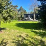 Moderne Villa mit Terrasse und Garten. Umgeben von Bäumen unter blauem Himmel.